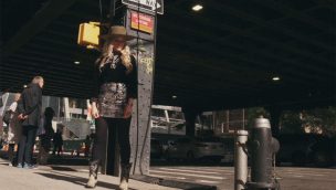 girl in new york city in boots standing in front of a stop light with a crowd behind her